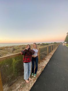 two women standing next to each other on the side of a road near the ocean