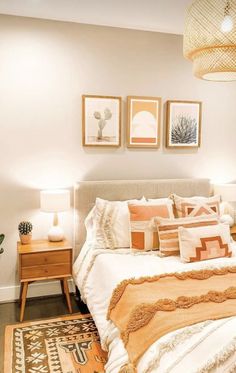 a bed with orange and white pillows on top of it next to two pictures above the bed