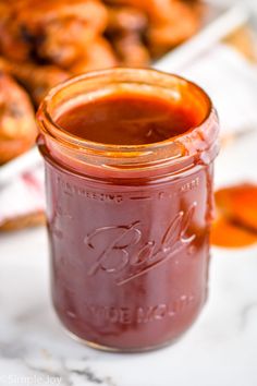 a jar of bbq barbecue sauce sitting on a table with muffins in the background