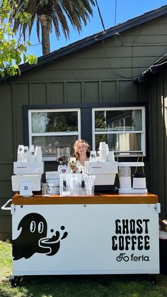 a woman standing behind a coffee cart with cups on the table and an advertisement for ghost coffee