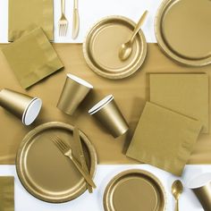 the table is set with gold paper plates and silverware, napkins and forks