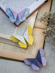 three origami butterflies sitting on top of an open book next to some flowers