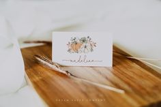 a place card sitting on top of a wooden table next to a white napkin and some feathers