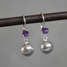 "These stunning sterling silver earrings feature a natural faceted amethyst gemstone and a dangling 8mm ball. The ear wires of these  earrings are securely soldered to the bezel, ensuring durability and comfort. The open back bezel design allows light to pass through, enhancing the brilliance of the gemstone. The earrings have a polished finish for a sleek and shiny appearance. These versatile earrings are perfect for any occasion, whether it's for everyday wear, office attire, or an evening outing. They also make a wonderful gift for someone special or as a treat for yourself.  Amethyst is the birthstone for the month of February and the 6th and 17th wedding anniversaries. The purple colour stone has long been a symbol of peace and calming energy. Amethyst is said to strengthen relationsh Peace And Calming, Symbol Of Peace, Colour Stone, Purple Colour, Ball Earrings, Sterling Silver Drop Earrings, Heart Dangle Earrings, Office Attire, Small Earrings