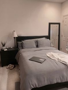 a laptop computer sitting on top of a bed next to a night stand and lamp