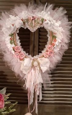 a heart shaped wreath with pink flowers and lace on it, hanging from a window sill