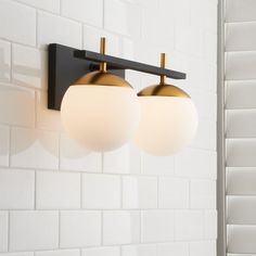 two light fixtures mounted on the wall in a bathroom with white tile and black accents