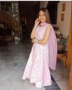 a woman in a pink and white dress is talking on her cell phone while wearing a shawl