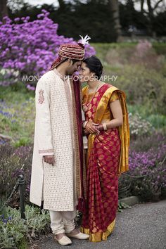 two people standing next to each other in front of purple flowers