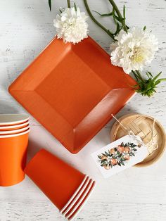 an orange plate with flowers on it next to other plates and utensils