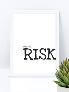 a plant is next to a white framed print with the words take the risk on it