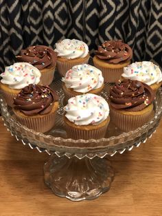 cupcakes with chocolate frosting and sprinkles on a glass cake plate