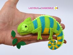 a hand holding a small green and blue toy chamelon on a tree branch