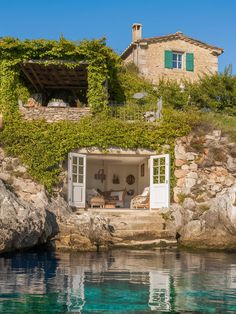 the house is surrounded by rocks and greenery on the cliff above the water's edge