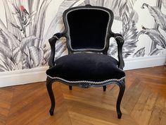 a black chair sitting on top of a wooden floor next to a wall with birds painted on it