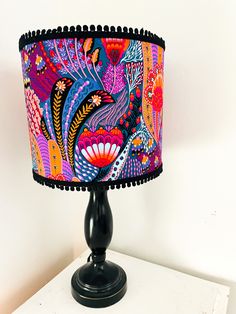 a colorful lamp shade sitting on top of a wooden table next to a white wall