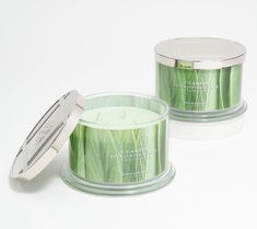 two green candles sitting next to each other on a white surface with a silver lid