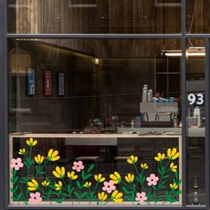 a window with flowers painted on it in front of a counter and coffee shop sign