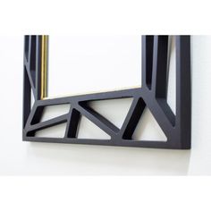 a mirror that is on the wall with black and gold trimmings, in front of a white wall