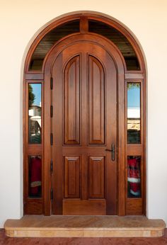 an arched wooden door with two red pillows on the steps and a white wall behind it