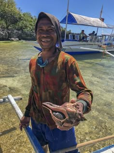 a man standing on top of a boat holding an animal in his hands and smiling