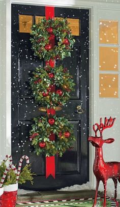 a christmas tree decorated with red and green ornaments next to a black door in the snow