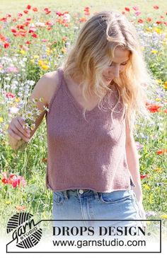 a woman standing in a field of flowers with her hand on her hip and looking down at the ground