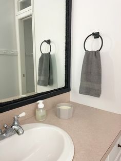 a bathroom sink sitting under a mirror next to a white counter top with two towels hanging on it