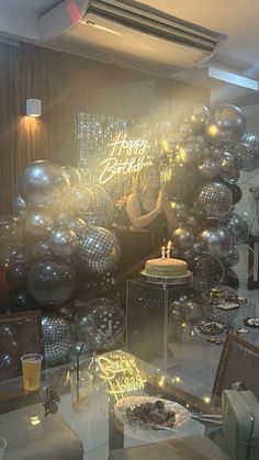 a woman sitting in front of a birthday cake surrounded by balloons