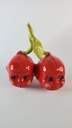 two red plastic cherries sitting on top of each other next to a green leaf