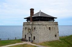 an old stone tower with a clock on the top and water in the back ground