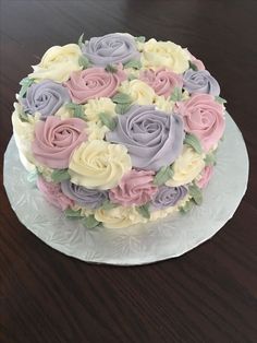 a cake decorated with pastel roses on a glass plate sitting on a wooden table