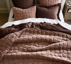 a bed with brown and white comforters on it's sides, next to a night stand