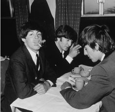 three men sitting at a table with cups and saucers in front of their mouths