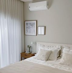 a bed with white sheets and pillows next to a wall mounted air conditioner in a bedroom