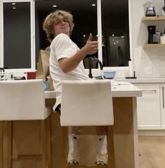 a young man sitting at a kitchen counter making a gesture with his hand in the air