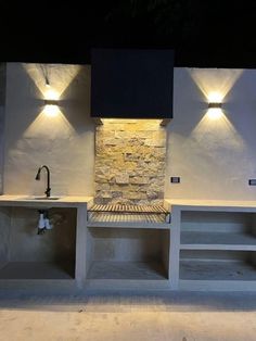 an outdoor kitchen with stone counters and lights on the back wall, along with built - in shelving