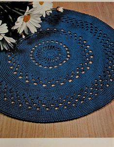 a crocheted doily with daisies on a wooden table next to it