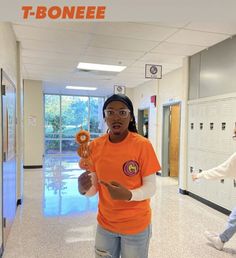 a woman in an orange t - shirt is holding a donut and standing in a hallway