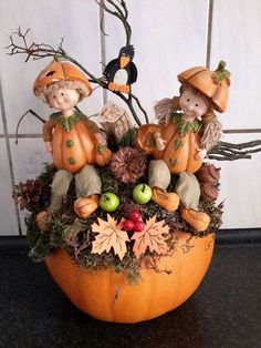 two figurines sitting on top of a pumpkin filled with leaves and acorns