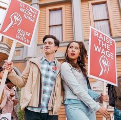 a man and woman holding signs in front of a building while standing next to each other