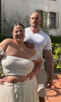 a man and woman standing next to each other in front of a building with potted plants