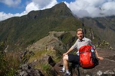 a man sitting on top of a mountain next to a red bag