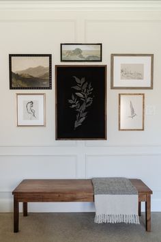 a wooden bench sitting in front of a wall with pictures hanging on it's side