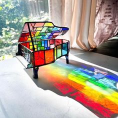 a multicolored piano sitting on top of a white table next to a window