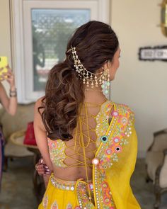 a woman in a yellow outfit with jewelry on her neck and back, looking at the mirror