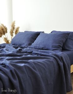 an unmade bed with blue linens and dried flowers on the nightstand next to it