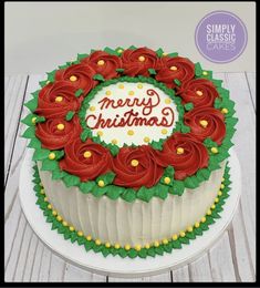 a cake decorated with red roses and green leaves is on a white plate that says merry christmas