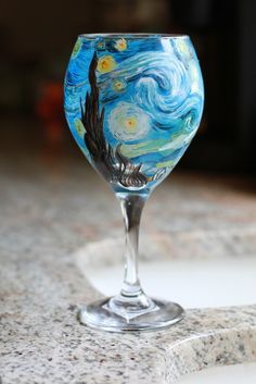 a wine glass sitting on top of a counter next to a marble slab with an image of the starry night