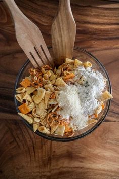 a bowl filled with pasta and cheese next to two wooden utensils on top of a table